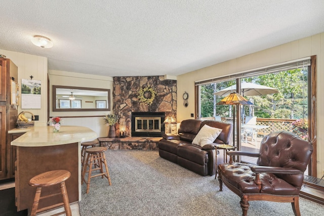 living room with a textured ceiling, carpet flooring, and a stone fireplace