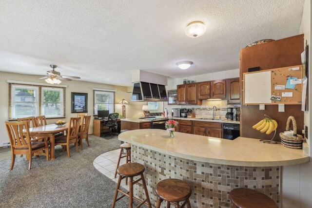 kitchen with black dishwasher, light countertops, a sink, a peninsula, and a kitchen bar