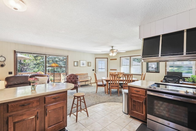 kitchen with light countertops, light tile patterned flooring, ceiling fan, a textured ceiling, and stainless steel range with electric stovetop