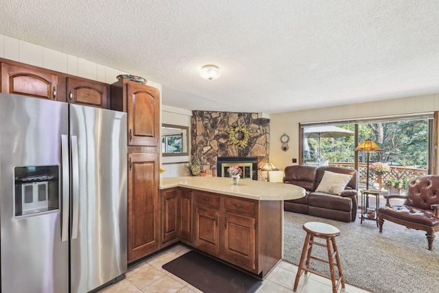 kitchen with light countertops, open floor plan, a stone fireplace, stainless steel fridge, and a peninsula