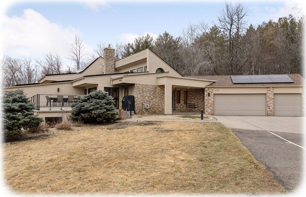 view of front of home with solar panels, concrete driveway, a chimney, an attached garage, and a front yard