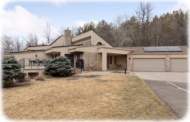 view of front of home with solar panels, concrete driveway, a chimney, an attached garage, and a front yard