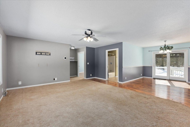 carpeted empty room with a textured ceiling, ceiling fan with notable chandelier, wood finished floors, and baseboards