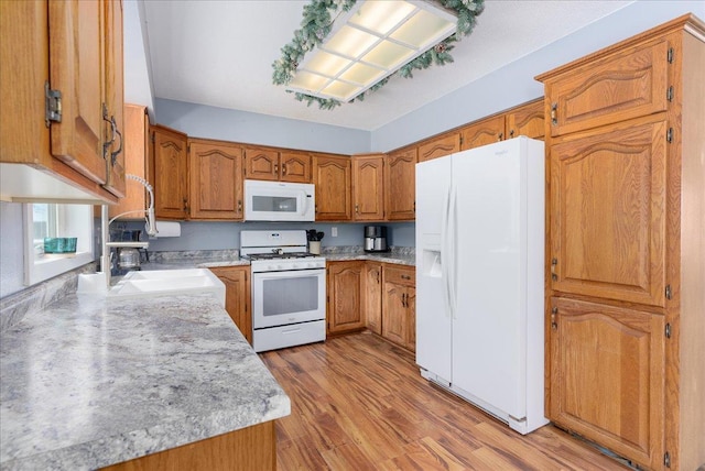 kitchen with brown cabinets, light countertops, light wood-style flooring, a sink, and white appliances