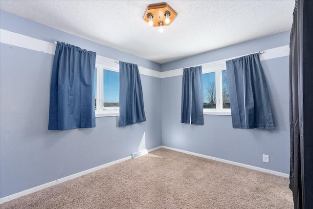 carpeted spare room featuring baseboards, a textured ceiling, and a healthy amount of sunlight