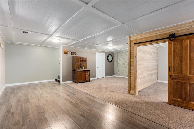 finished basement with a barn door, wood walls, visible vents, baseboards, and light wood finished floors