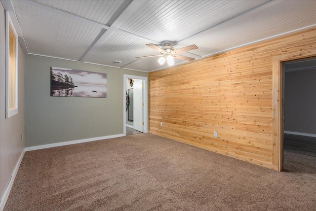 carpeted empty room with wood walls, baseboards, and a ceiling fan