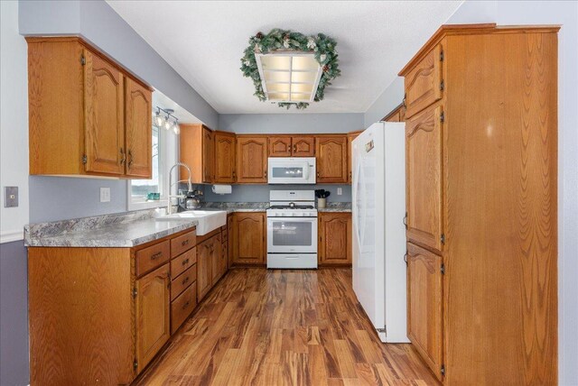 kitchen with brown cabinets, light countertops, a sink, wood finished floors, and white appliances