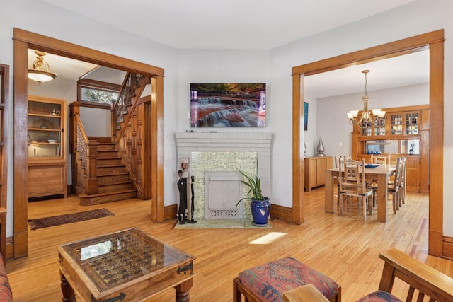 living room featuring a notable chandelier, stairway, light wood finished floors, baseboards, and a brick fireplace