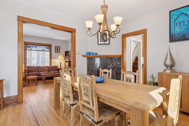 dining area with stairway, an inviting chandelier, light wood-style floors, and a premium fireplace