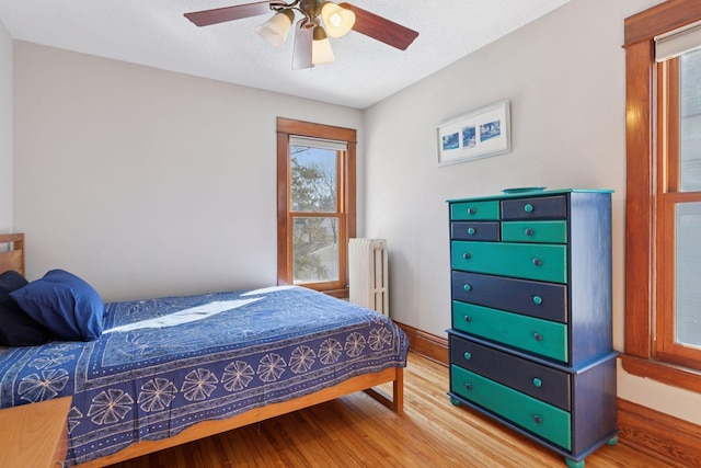 bedroom with light wood-type flooring, a textured ceiling, radiator heating unit, baseboards, and ceiling fan