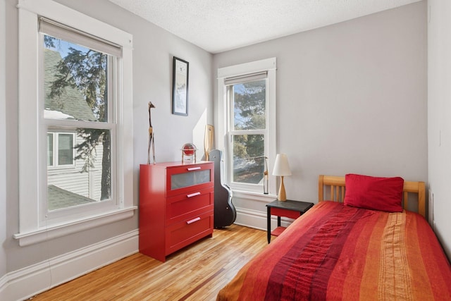 bedroom featuring multiple windows, baseboards, light wood finished floors, and a textured ceiling