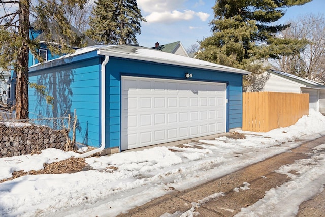 snow covered garage featuring a detached garage and fence