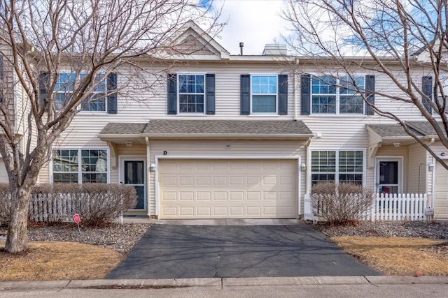 townhome / multi-family property featuring a garage, roof with shingles, driveway, and fence