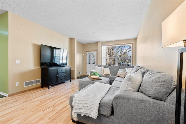 living area featuring baseboards, visible vents, a textured ceiling, and light wood finished floors