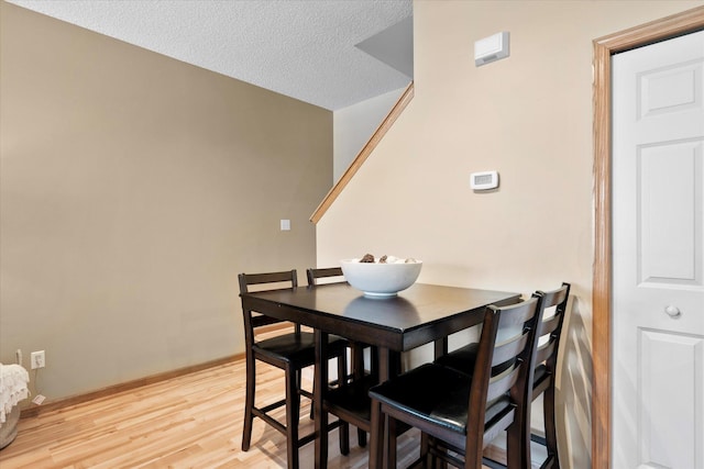 dining space with a textured ceiling, light wood-type flooring, and baseboards