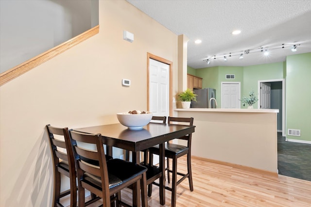 dining room with a textured ceiling, light wood-style flooring, visible vents, and baseboards