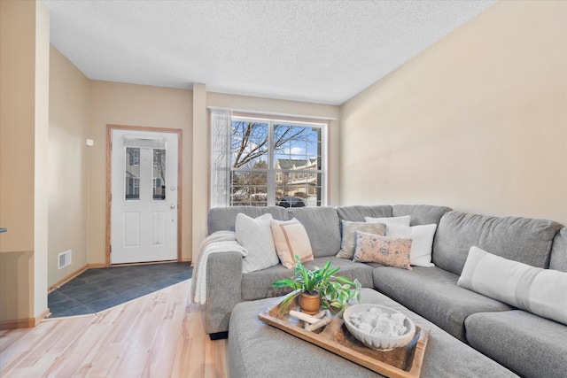 living area with a textured ceiling, wood finished floors, visible vents, and baseboards