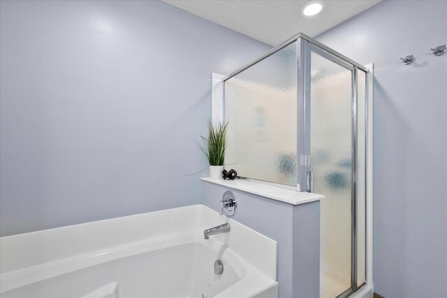 full bath with a garden tub, a textured ceiling, and a shower stall