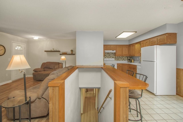 kitchen featuring white appliances, a breakfast bar, decorative backsplash, light countertops, and under cabinet range hood