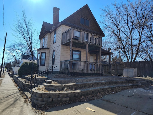 view of front facade with a porch, a chimney, fence, and a balcony