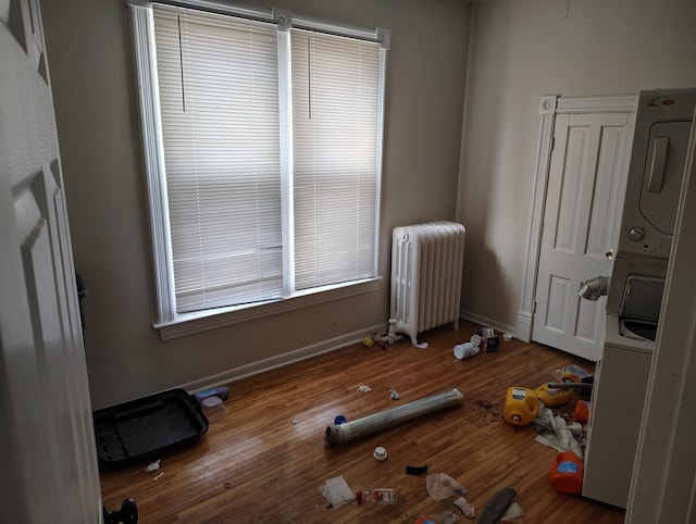 exercise area with baseboards, stacked washing maching and dryer, radiator heating unit, and wood finished floors