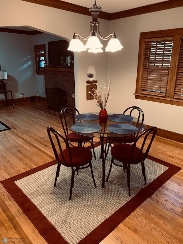 dining room with crown molding, a fireplace, light wood-style flooring, and baseboards