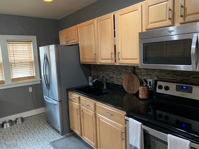 kitchen featuring light brown cabinets, a sink, baseboards, appliances with stainless steel finishes, and decorative backsplash