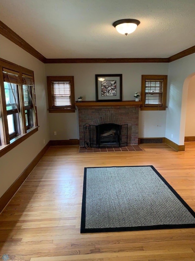 unfurnished living room with arched walkways, ornamental molding, a brick fireplace, wood finished floors, and baseboards