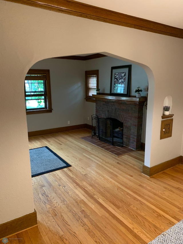 unfurnished living room featuring a brick fireplace, baseboards, arched walkways, and wood finished floors