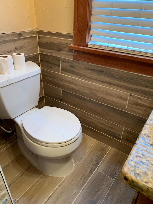 bathroom featuring a wainscoted wall, toilet, and tile walls