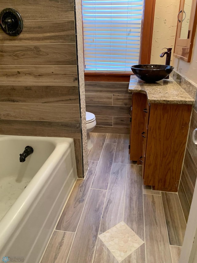 bathroom with a tub to relax in, wood tiled floor, vanity, and toilet