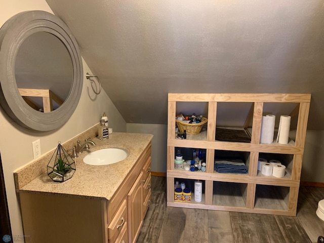 bathroom with vaulted ceiling, vanity, a textured ceiling, wood finished floors, and baseboards