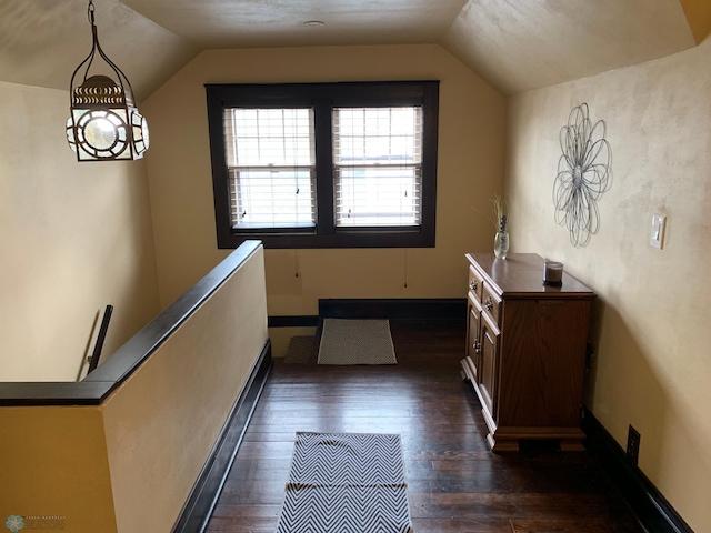 corridor featuring dark wood-type flooring, vaulted ceiling, and baseboards