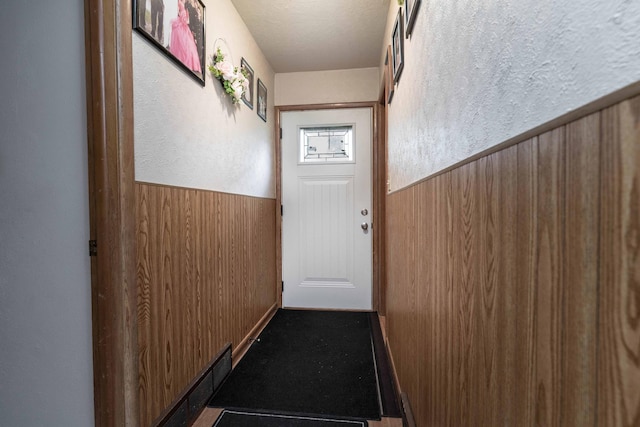 doorway featuring a textured wall, wainscoting, wood walls, and a textured ceiling