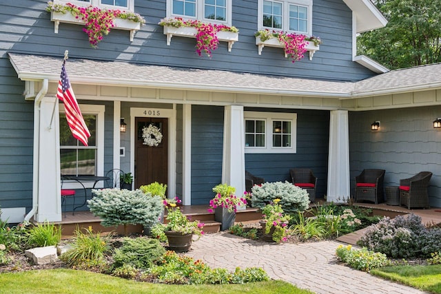 view of exterior entry with a porch and a shingled roof