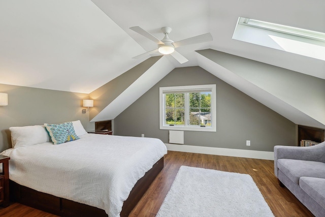 bedroom featuring a ceiling fan, vaulted ceiling with skylight, wood finished floors, and baseboards