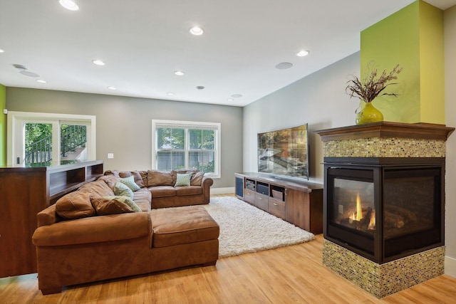 living room featuring baseboards, a multi sided fireplace, light wood-style floors, and recessed lighting