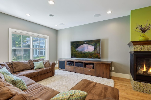 living room with a glass covered fireplace, recessed lighting, light wood finished floors, and baseboards