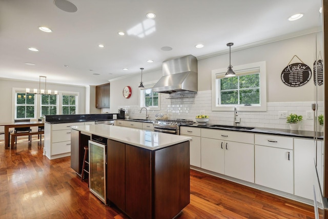 kitchen with ornamental molding, wine cooler, a sink, and wall chimney range hood