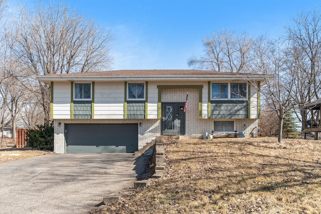 raised ranch featuring aphalt driveway, an attached garage, and brick siding