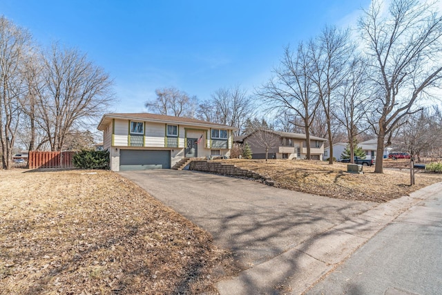 bi-level home featuring an attached garage, fence, brick siding, and driveway