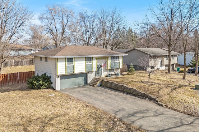 bi-level home with brick siding, an attached garage, driveway, and fence