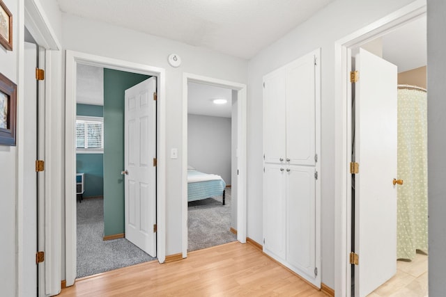 hall featuring light wood finished floors, a textured ceiling, and baseboards