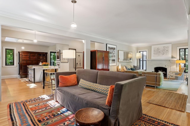 living area with baseboards, light wood-style floors, a brick fireplace, and crown molding