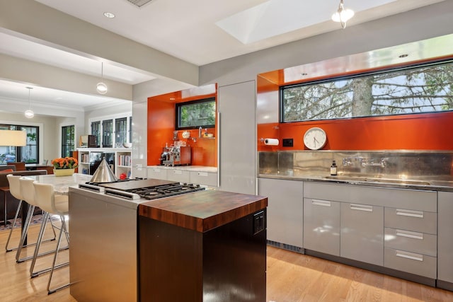 kitchen with a skylight, stainless steel gas range oven, a kitchen breakfast bar, light wood-type flooring, and butcher block counters