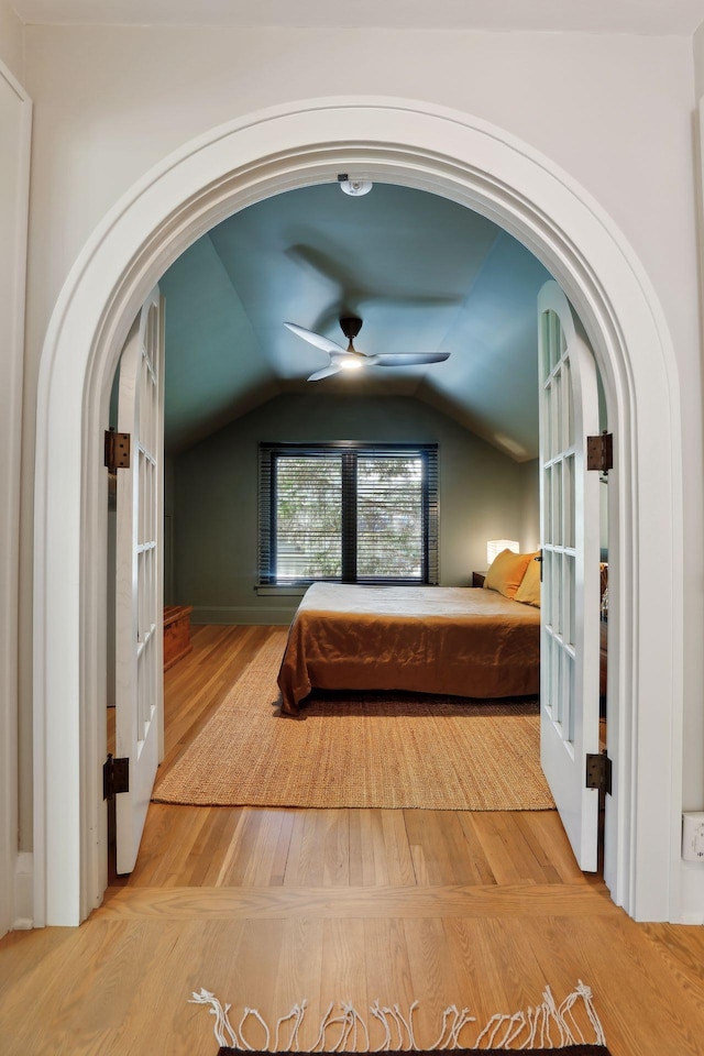 unfurnished bedroom featuring arched walkways, vaulted ceiling, a ceiling fan, and wood finished floors