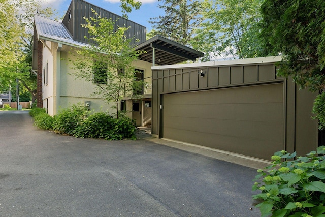 view of front facade featuring board and batten siding, aphalt driveway, stucco siding, metal roof, and an attached garage