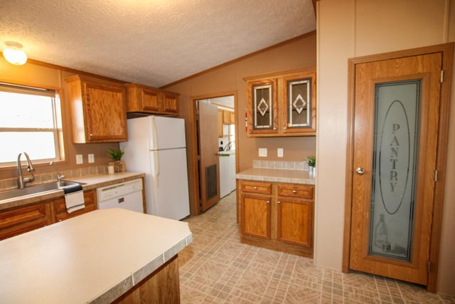 kitchen featuring lofted ceiling, white appliances, a sink, light countertops, and brown cabinets