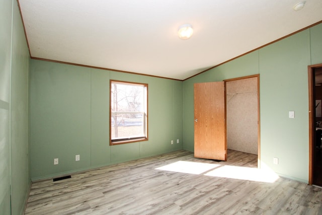 unfurnished bedroom with lofted ceiling, visible vents, crown molding, and wood finished floors